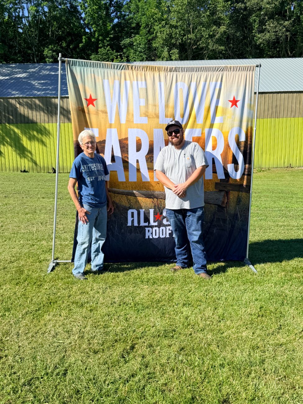 A customer and crew member at the We Love Farmers banner