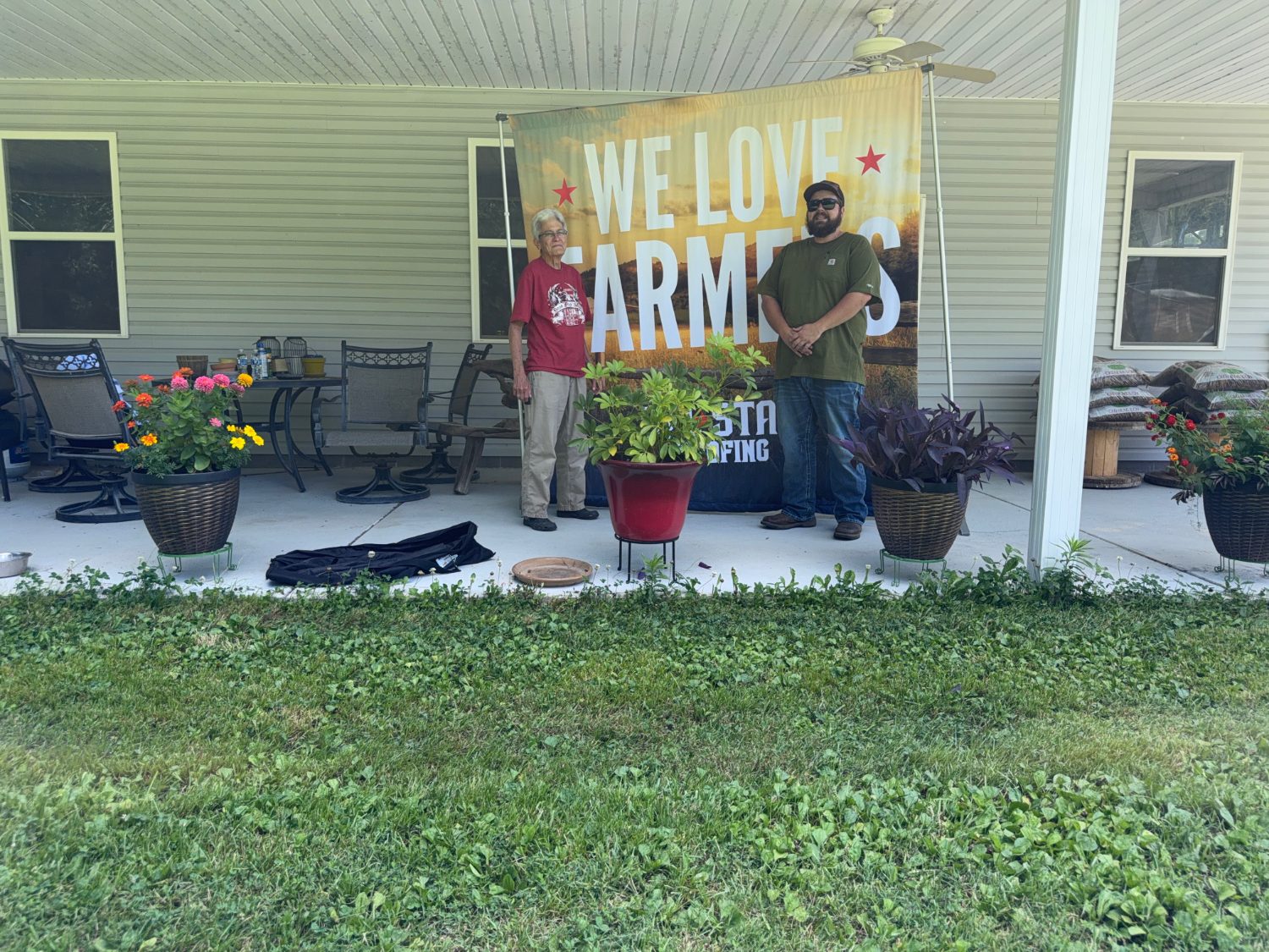 A front-porch visit with a customer beside the We Love Farmers banner